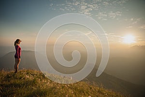 Woamn stands on a peak of mountain at sunset