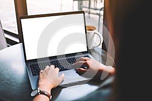 A woamn using and typing on laptop with blank white desktop screen with coffee cup on the table