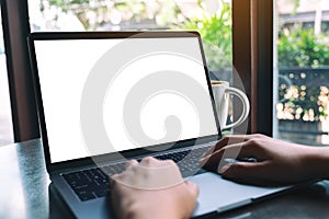 A woamn using and typing on laptop with blank white desktop screen with coffee cup on the table