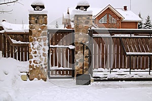 Wodden fence and brick gate covered with snow.