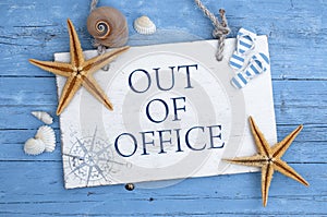 Wodden sign with message out of office with mediterranean decorative items on blue weathered background