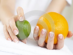 Woiman`s Hands with French Manicure on Nails Holding a Fresh Summer Orange and Limet Fruits