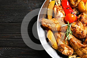Wok with barbecued chicken wings and garnish on wooden background, top view
