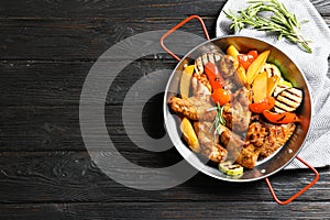 Wok with barbecued chicken wings and garnish on wooden background, top view.