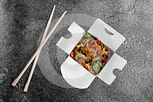 Wok in box rice noodles in black food container. Fast food delivery service. Takeaway chinese street meal.