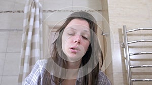 Woken tired woman in the bathroom smacks herself on the cheeks to wake up.