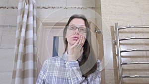 Woken tired woman in glasses in the bathroom smacks herself on the cheeks to Wake up.