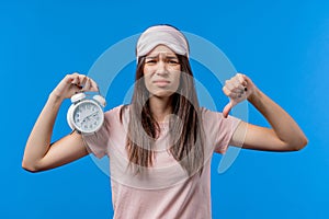 Woken up by alarm clock sleepy woman holding it in hand. Blue background. Early 7 o'clock in morning. Lazy lady