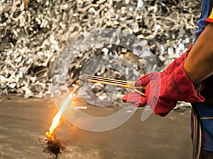 Woker holding metal cutting torch with soot and flame in recycle factory