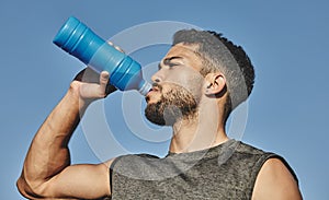 Woking up a thirst after an intense workout. Low angle shot of a sporty young man drinking water while exercising