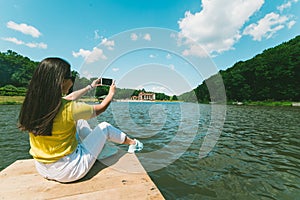 Womam sitting on a lake pier and taking picture