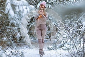 Woman 30-35 years old in a warm tracksuit on the background of a snowy forest with Christmas trees