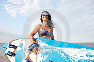 Woman 40-45 years old, walking along the beach against the background of water and beach umbrellas with a surfboard