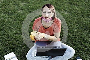 Woman 40 years old working outdoors with laptop during coronavirus outbreak - Smiling female entrepreneur sitting on lawn with pc