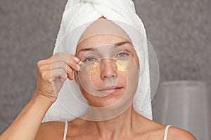 Woman of 40s after shower with towel on head with gold patches under eyes on face