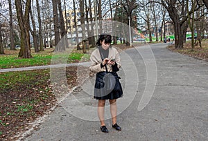 Woman, 45-year-old European woman with long dark hair stands in the park on the alley and looks at a mobile phone