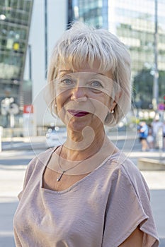Woman 65-70 years old with white hair on the background of a busy city street.