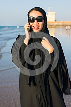 Woman in abaya using phone on the beach