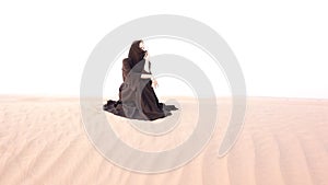 A woman in abaya sitting in the desert.
