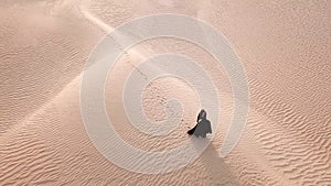 A woman in abaya walking in the desert.