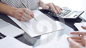 Woman accountant counting and discussing taxes with a client or a colleague while using a calculator and laptop computer