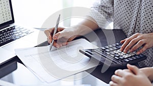 Woman accountant using a calculator and laptop computer while counting taxes for a client. Business audit concepts