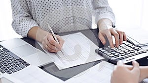 Woman accountant using a calculator and laptop computer while counting taxes with a client or a colleague. Business