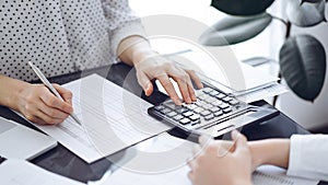 Woman accountant using a calculator and laptop computer while counting taxes with a client or a colleague. Business