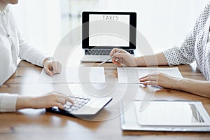 Woman accountant using a calculator and laptop computer while counting taxes with colleague at wooden desk in office