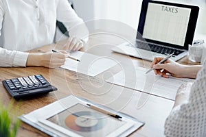 Woman accountant using a calculator and laptop computer while counting taxes with colleague at wooden desk in office