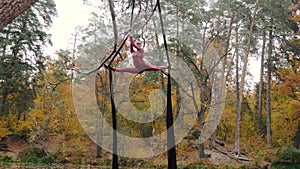 Woman acrobat hanging on the aerial silk and shows a show of air acrobatics in the forest.