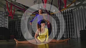 Woman acrobat sits on a string, the other stands on her arms from above