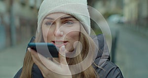 Woman activates smartphone digital virtual app voice assistant recording audio messages at outdoor. Young Girl in hat