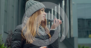 Woman activates smartphone digital virtual app voice assistant recording audio messages at outdoor. Young redhead Girl