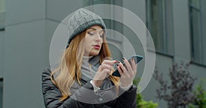 Woman activates smartphone digital virtual app voice assistant recording audio messages at outdoor. Young redhead Girl