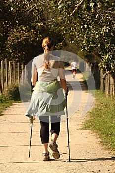 Woman in activewear and walking sticks is walking down a path of dirt.