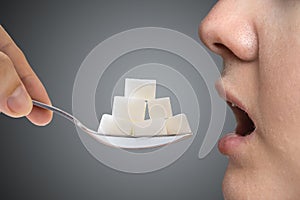 Woman addicted on sugar is eating spoon full of sugar blocks. Unhealthy eating concept