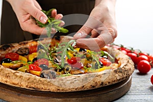 Woman adding arugula to vegetable pizza at table