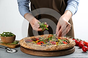 Woman adding arugula to vegetable pizza at table