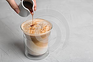 Woman adding caramel syrup to latte macchiato on table
