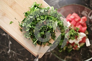 woman adding chopped greens to vegetable salad close-up