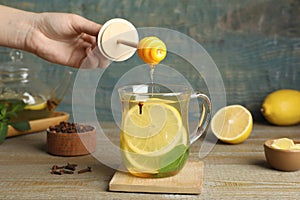 Woman adding honey to immunity boosting drink at wooden table, closeup