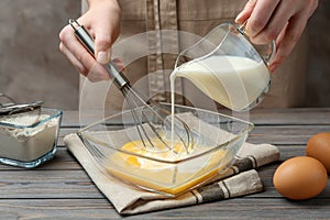 Woman adding milk to whisked eggs at wooden table, closeup photo