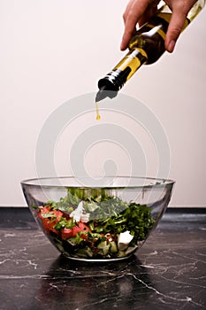 woman adding olive oil to vegetable salad close-up of hands