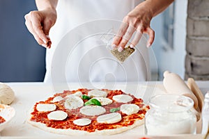 Woman adding oregano on raw pizza.