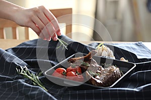 Woman adding rosemary to roasted ribs at table, closeup