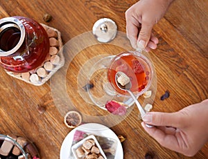 Woman adding sugar to a red berry tea. Top view of buttered cookies and tea kettle. Sweet breakfast. Cosiness concept.