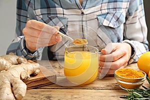 Woman adding turmeric to immunity boosting drink at wooden table with ingredients  closeup