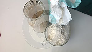 A woman adds flour to a glass of water. Makes a mixture for feeding bread sourdough. Sourdough stands next to a glass jar.