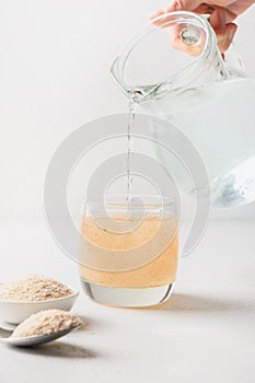 Woman adds psyllium fiber to glass of water on a white background.